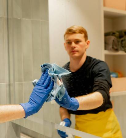 close up in an apartment cleaner in a yellow apron is cleaning mirror with a rubber brush close up in an apartment a cleaner in a yellow apron is cleaning mirror with a rubber brush